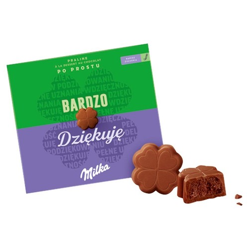 Praliny Milka w pudełku z napisem "Po prostu bardzo dziękuję". Obok dwie czekoladowe koniczynki, jedna przekrojona, ukazująca ciemne nadzienie.