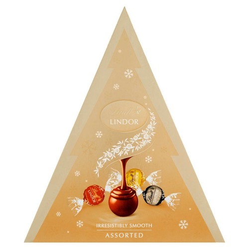 Opakowanie prezentowe Lindt Lindor Assorted w kształcie choinki. Na beżowym tle widoczne są białe płatki śniegu i gałązki. Grafika przedstawia czerwoną truflę z polewą oraz trzy opakowane czekoladki Lindor. Produkt to mieszanka smaków.