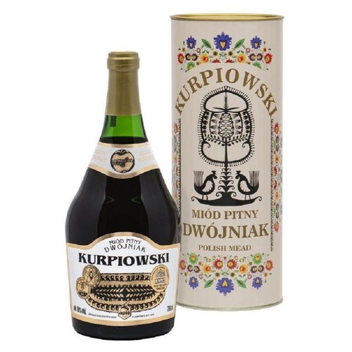 Butelka miodu pitnego Kurpiowski Dwójniak o pojemności 750 ml, z ciemnego szkła, z zieloną szyjką i złotą etykietą z napisem "Miód Pitny Dwójniak Kurpiowski". Obok stoi cylindryczne opakowanie z kolorowymi ludowymi wzorami kwiatów i ptaków.